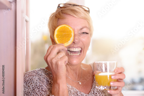 Lachende Frau hält eine Orangenscheibe an ihr Auge