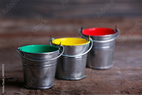 Metal buckets with colorful paint on wooden background © Africa Studio