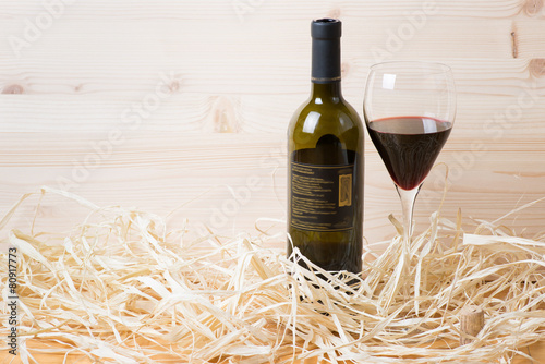 Bottle and glass of red wine with cork in straw