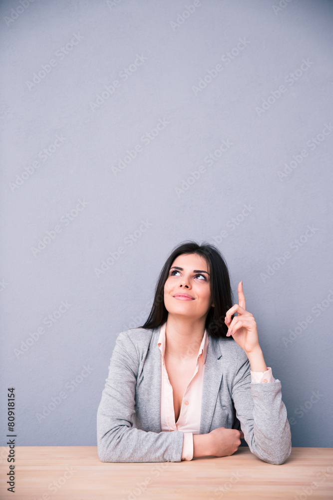 Thoughtful young woman sitting at the table and pointing up Thoughtful young woman sitting at the table and pointing up