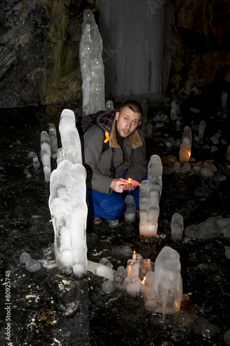 man with a burning candle sits in a cave with ice blocks