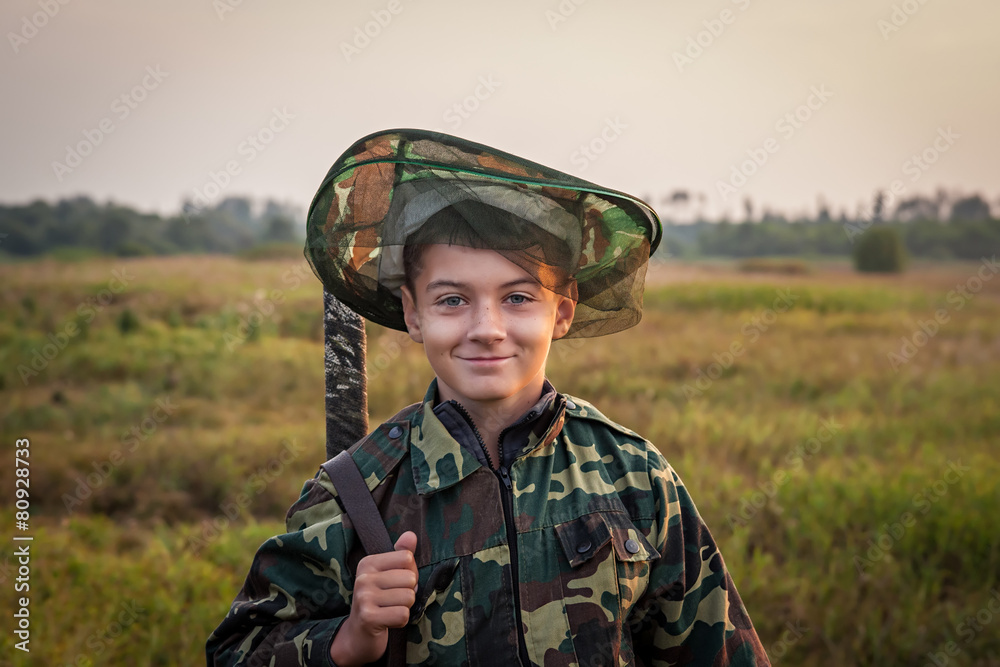 Young smiling boy with hunting shotgun standing at green field