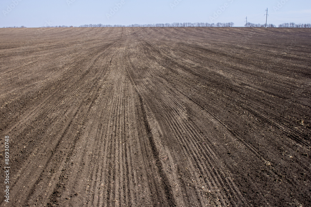 an image of black ploughed field under blue sky