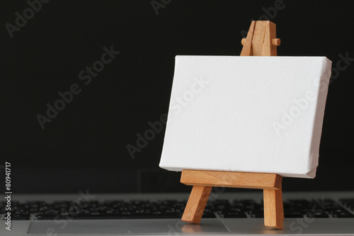 blank canvas and wooden easel on laptop computer as concept