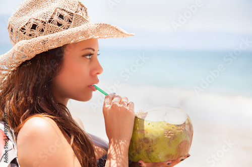 Frau trinkt Kokosnussmilch mit einem Strohhalm am Strand photo