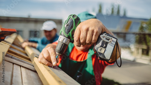 roofer using a drill is fastening a cap to a house roof photo