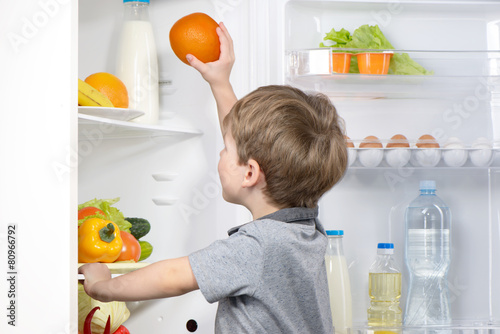 Little cute boy picking orange from fridge