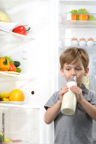 Cute boy drinking milk near open fridge