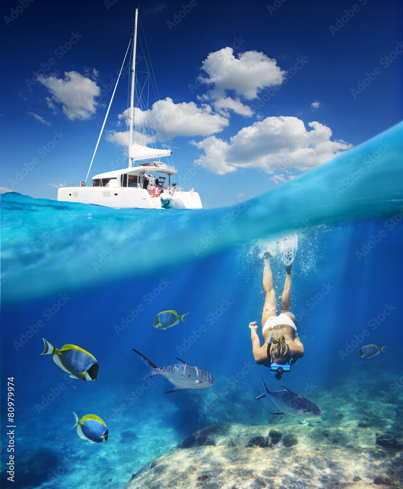 Girl diving in ocean with fishes next to catamaran at sunny day - obrazy, fototapety, plakaty 