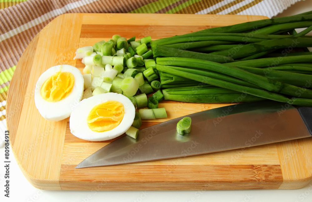Egg, cut in half, and green onion on the board. Egg, cut in half, and green onion on the board.