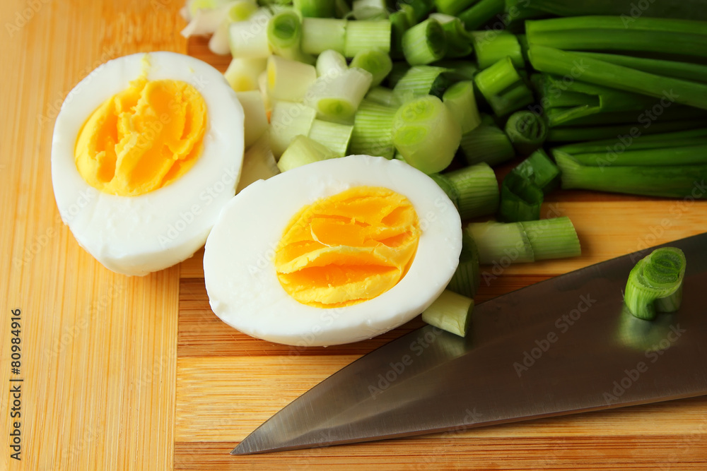 Egg, cut in half, and green onion on the board. Egg, cut in half, and green onion on the board.