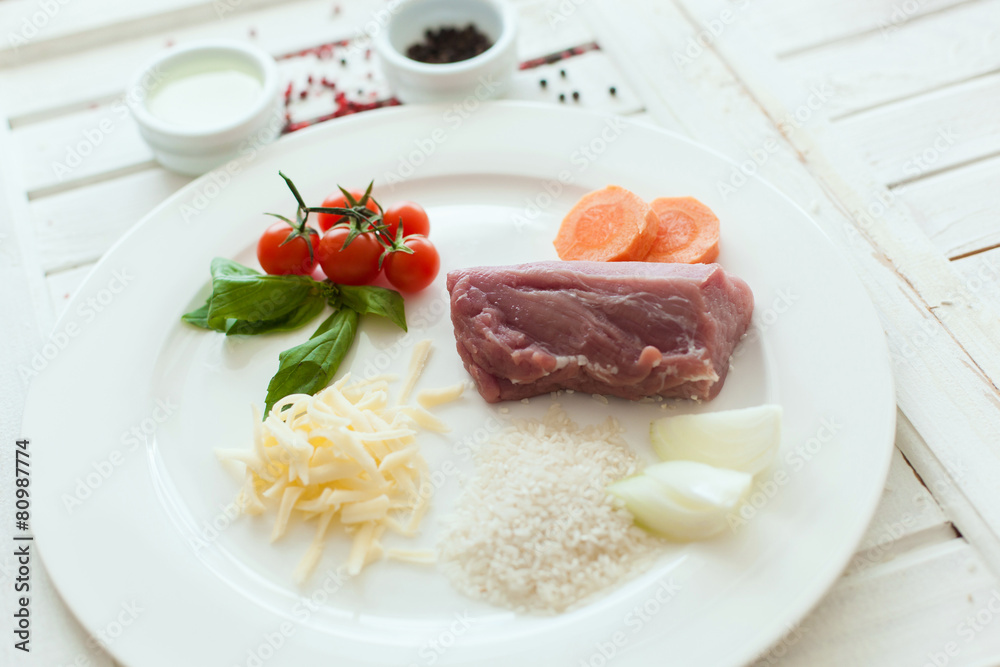 Ingredients to make a meal including meat, cherry tomatoes, cheese, sliced carrots, rice and spices on a white plate