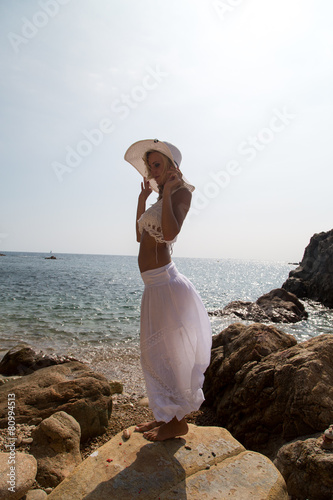 Lady in Hat and white lace dress on rocky beach. photo