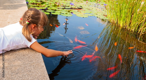 Little girl plays with ornamental fish that swim in  pond photo