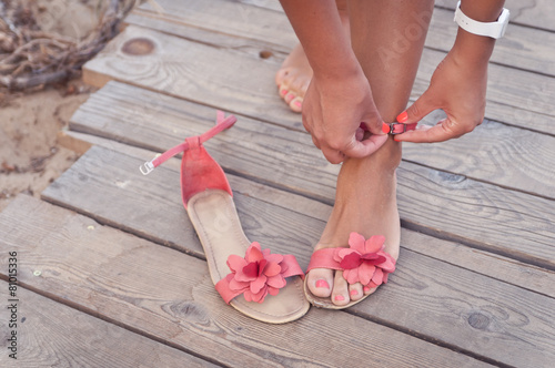 A girl putting on coral sandals at the beach sundeck