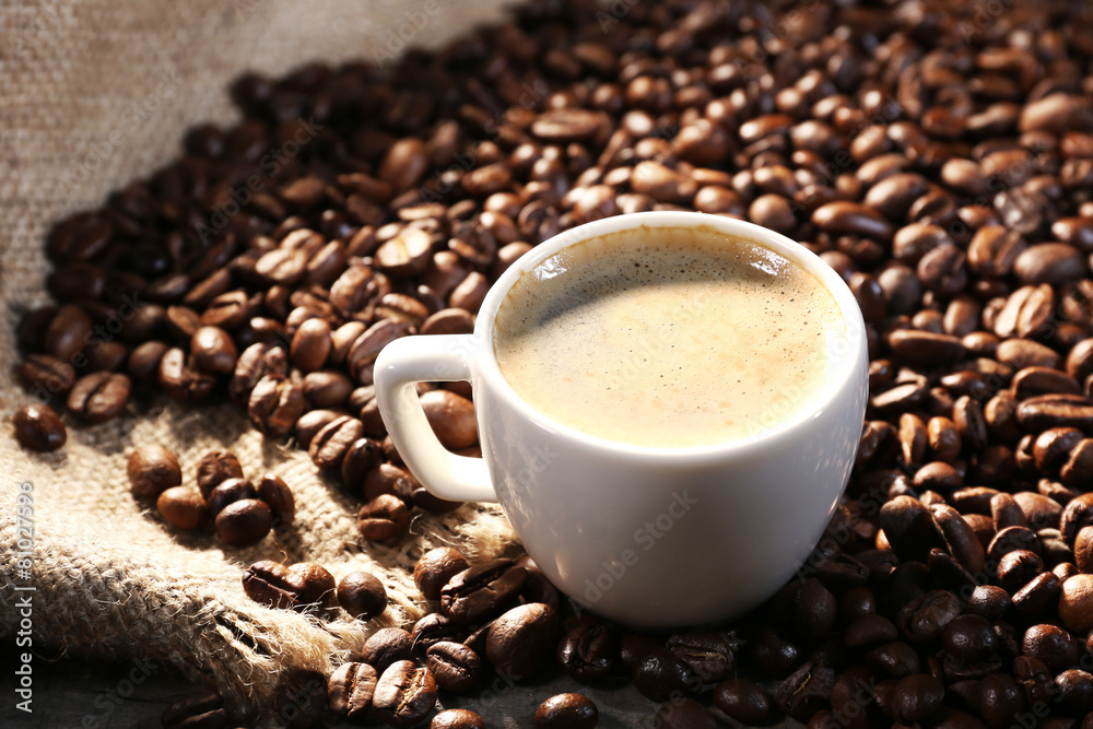 Cup of coffee and grains on wooden table with sackcloth,