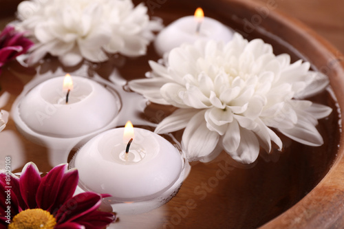 Bowl of spa water with flowers and candles, closeup