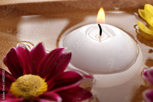 Bowl of spa water with flowers and candle, closeup