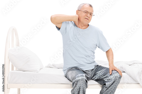 Senior man in pajamas feeling pain in his neck seated on a bed © Ljupco Smokovski
