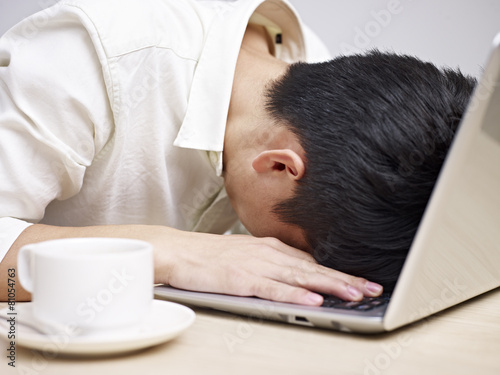 frustrated young man burying his head in keyboard of computer photo