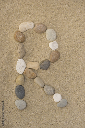 Buchstabe R aus Kieselsteinen im Sand