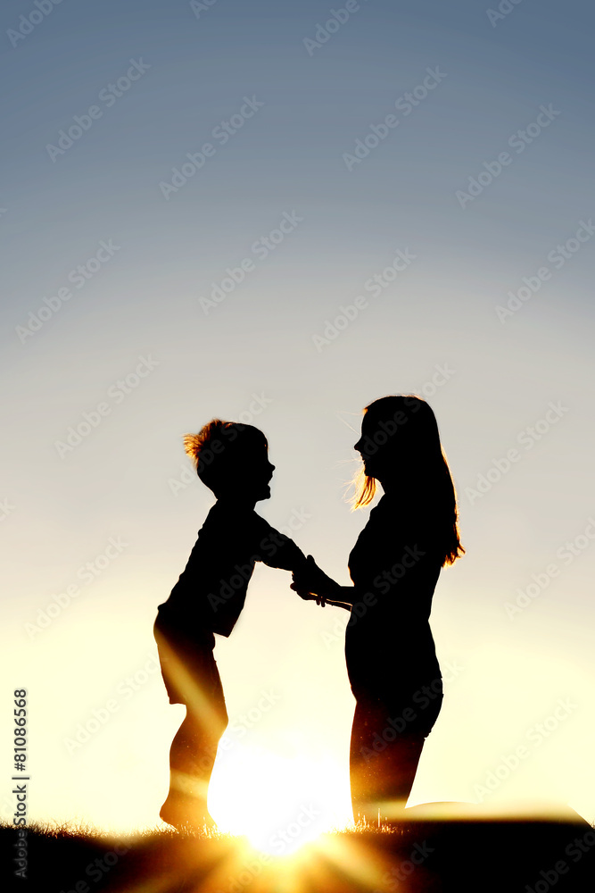 Fototapeta premium Silhouette of Mother and Young Child Holding Hands at Sunset