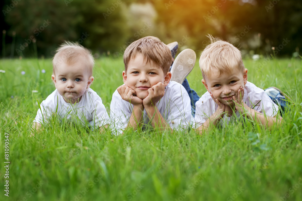 Three happy children brothers resting on the green grass in s Three happy children brothers resting on the green grass in s