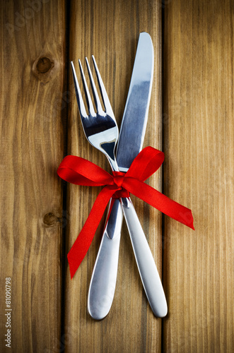 Top view of silver fork and knife decorated red ribbon