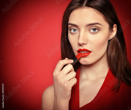 Beautiful young woman applying red lipstick on her lips. Toned.