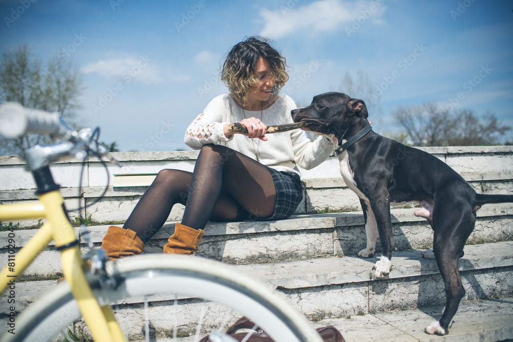 Beautiful young woman with bicycle playing with a dog