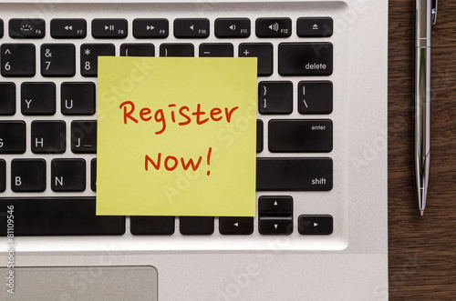 Notepad with words " Register Now " putting on laptop