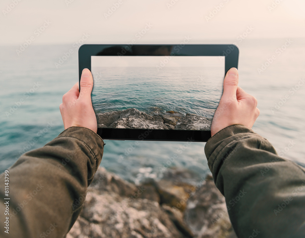 Woman photographs coast on tablet PC