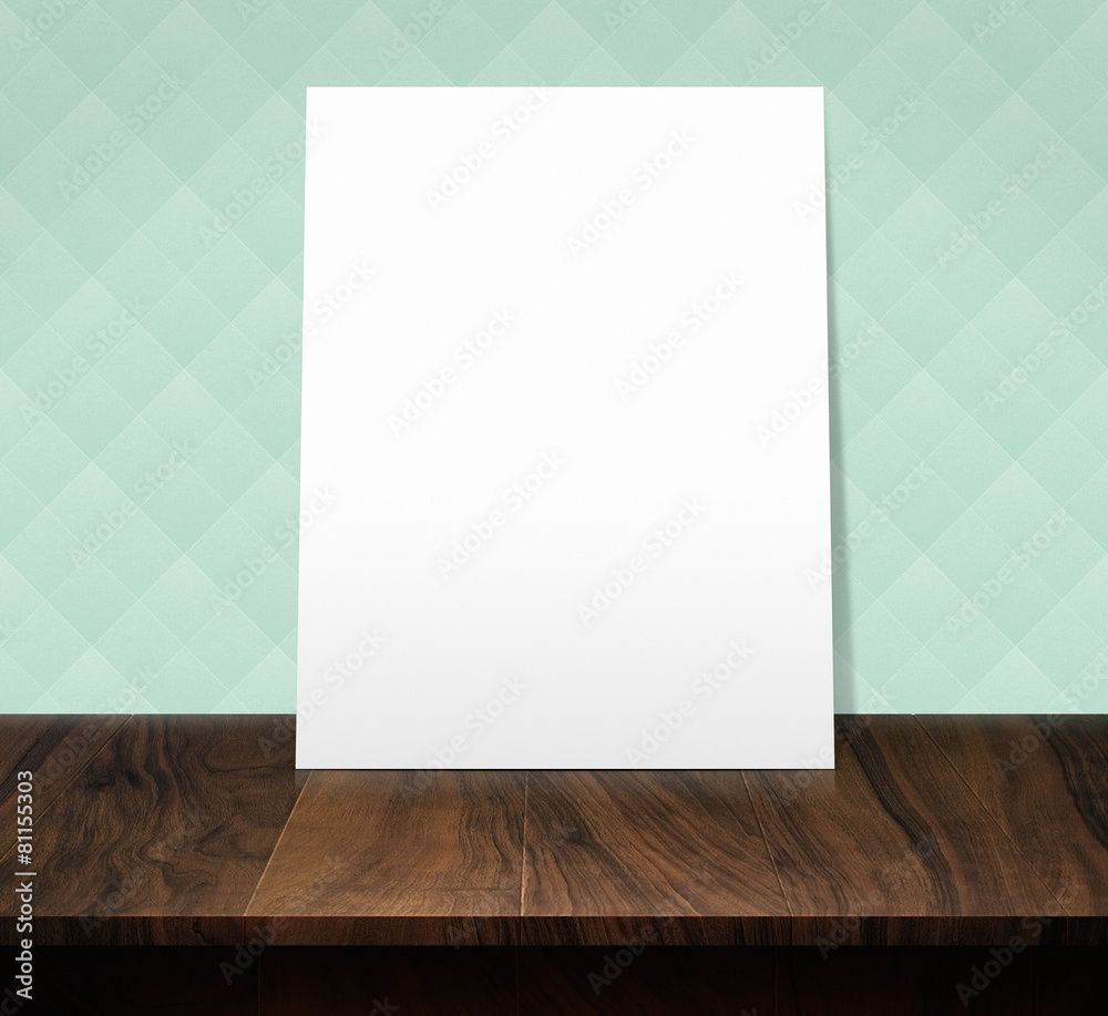 white poster on a wooden table with a green diamond pattern wall Stock