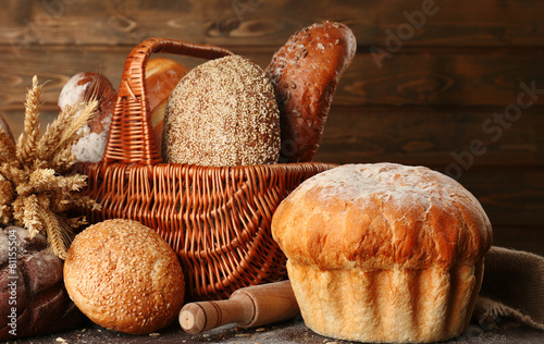 Different bread with ears in basket on wooden background