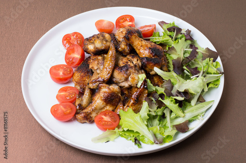 Chicken wings fried with honey decorated tomatoes and salad.