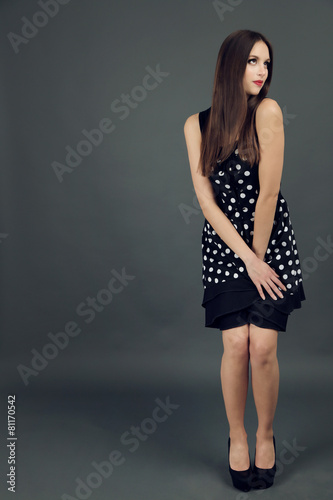 Beautiful young woman in dots dress on dark gray background