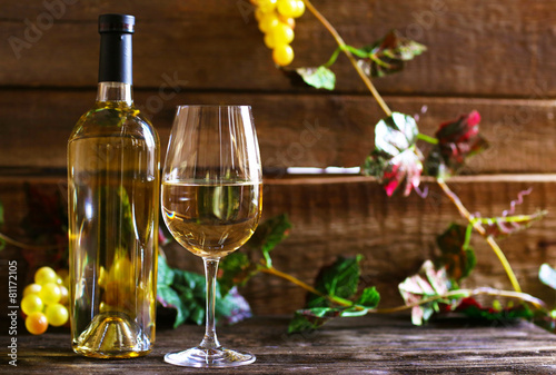 Bottle and glass of wine with grape on wooden background