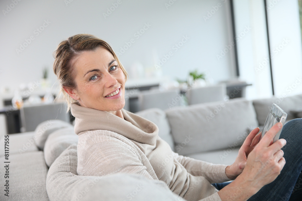 Mature woman sitting in sofa and websurfing with tablet Mature woman sitting in sofa and websurfing with tablet
