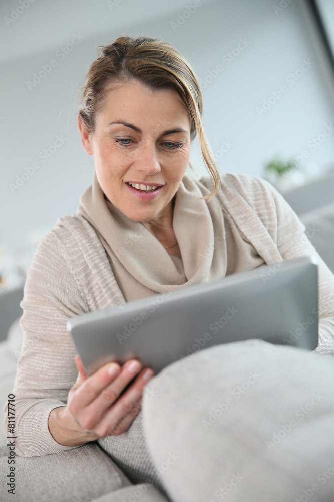 Mature woman sitting in sofa and websurfing with tablet Mature woman sitting in sofa and websurfing with tablet