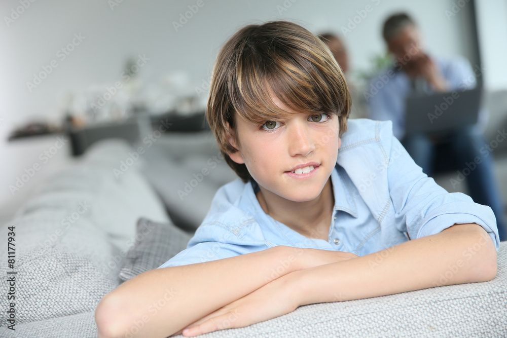 Portrait of teenage boy sitting in sofa, parents in background Portrait of teenage boy sitting in sofa, parents in background