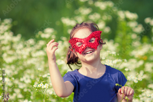 Happy little girl wearing a red mask on the flower meadow