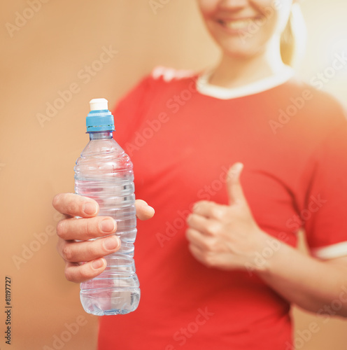 Young smilingl woman holding plastic bottle. Thumbs up. Focused