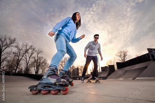 Girl on rollerblades and boy on skateboard in skate park photo
