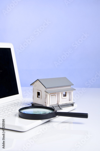 portrait of magnifying glass, model house and laptop