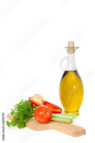 Olive oil in a glass jar and fresh vegetables on board