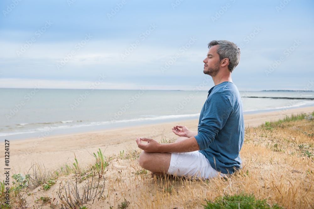 An attractive man is sitting face to the ocean in lotus position