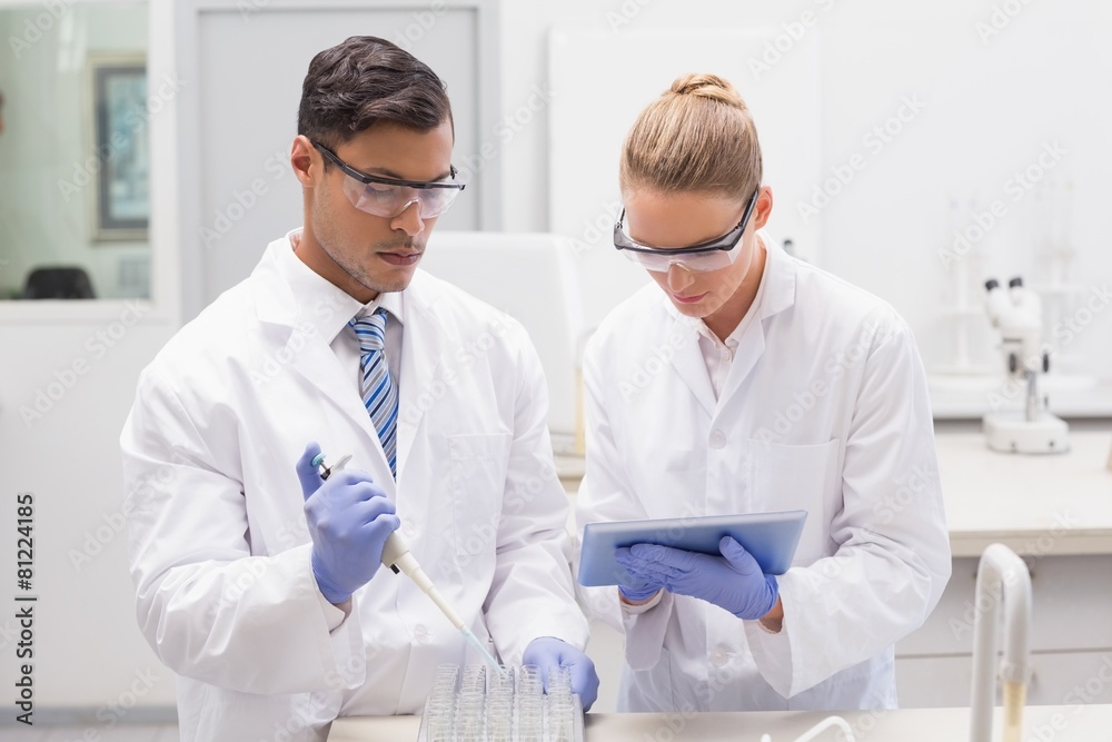 Scientists examining tubes in tray using tablet pc Scientists examining tubes in tray using tablet pc