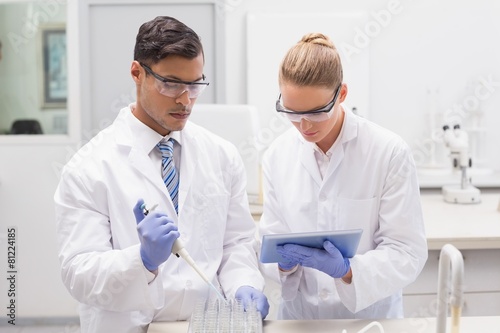Scientists examining tubes in tray using tablet pc
