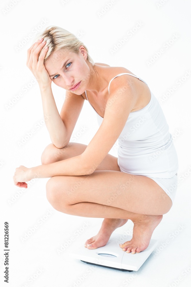 Sad woman squatting on scales looking at camera Sad woman squatting on scales looking at camera