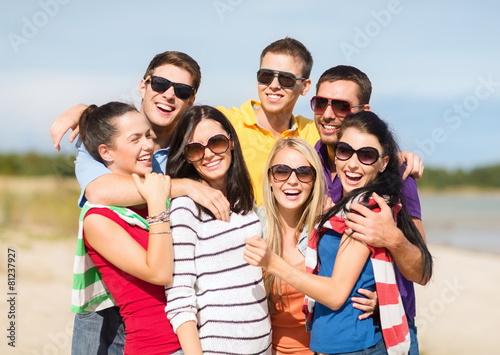 group of happy friends hugging on beach
